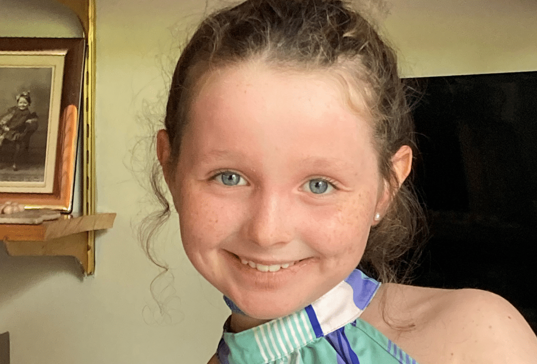 Close-up of a smiling young girl with curly hair, wearing a striped top.